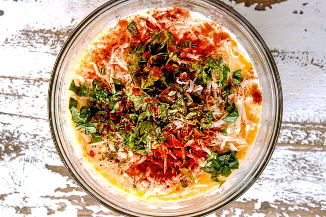 showing how to make egg frittata recipe by whisking together eggs, heavy cream, cheese and spices in a glass bowl