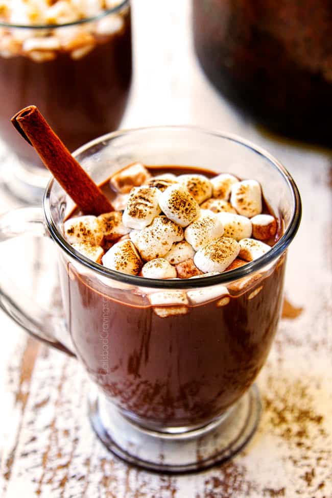 showing how to make hot chocolate recipe by adding hot chocolate to mug and adding marshmallows