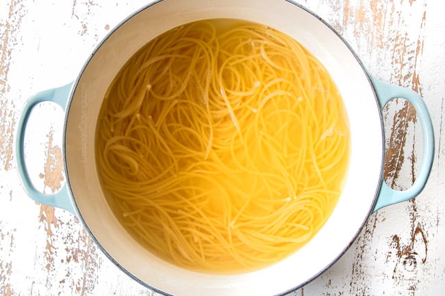 showing how to make spaghetti carbonara recipe by boiling spaghetti or bucatini in a Dutch oven with little water