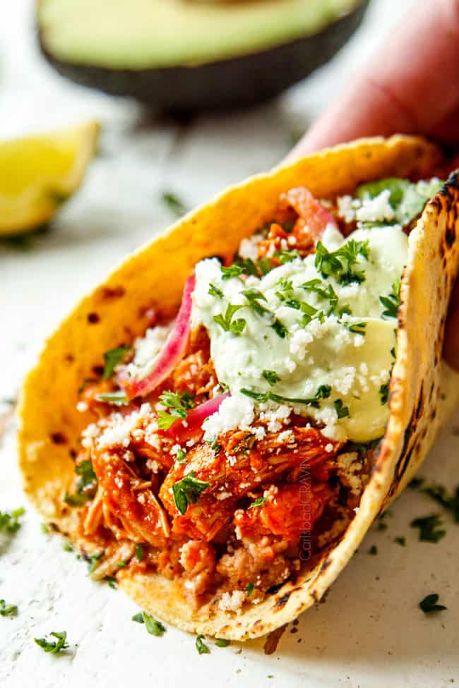 showing how to make chicken tinga tacos by adding chicken tinga to a corn tortilla