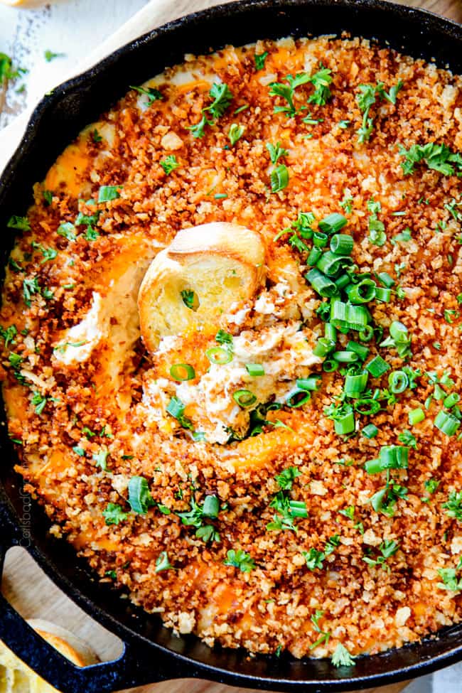 top view of hot crab dip recipe in a cast iron skillet with a dipper stuck into the center of the dip garnished with green onions.