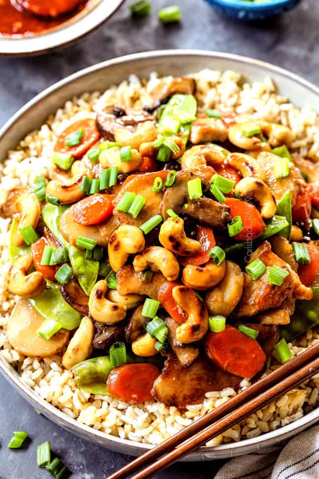 up close of serving Moo Goo Gai Pan in a bowl with rice garnished by green onions with chopsticks