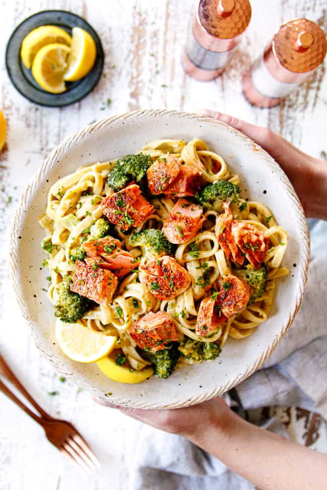 two hand holding a plate salmon pesto pasta recipe