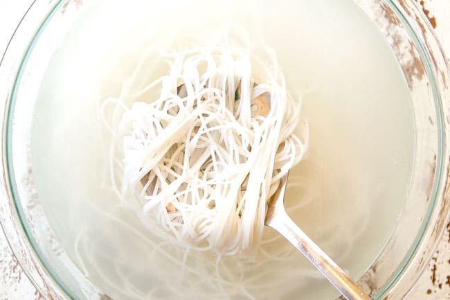 showing how to make Singapore Noodles by soaking rice vermicelli in hot water in a glass bowl