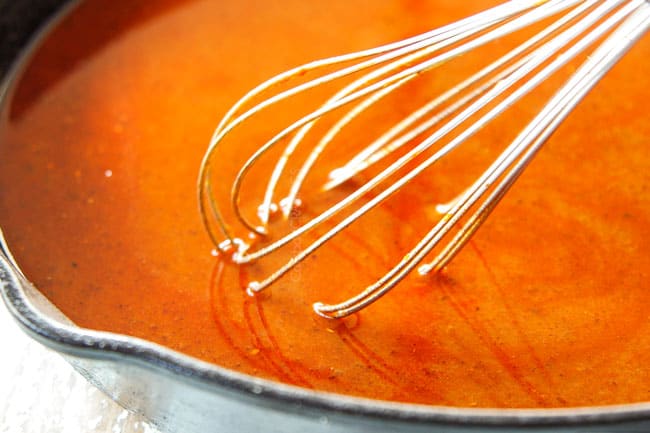 showing how to make enchilada sauce by whisking in tomato paste and chicken broth