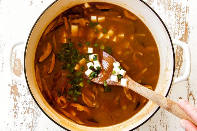 showing how to make hot and sour soup recipe by adding tofu and green onions and cornstarch slurry