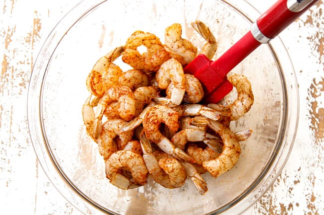 showing how to make Lemon Garlic Shrimp by seasoning the shrimp with salt, pepper and paprika in a glass bowl