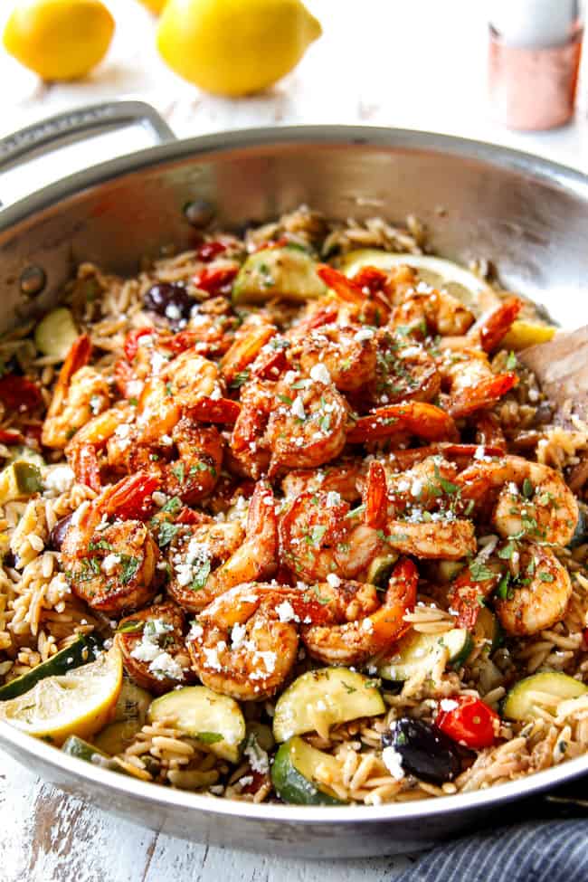 showing how to cook shrimp by tossing cooked lemon garlic shrimp with feta cheese