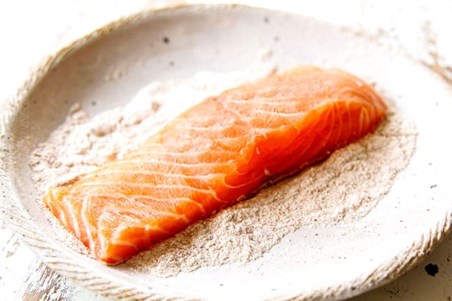 showing how to make lemon salmon and asparagus by adding salmon to shallow bowl with flour to dredge
