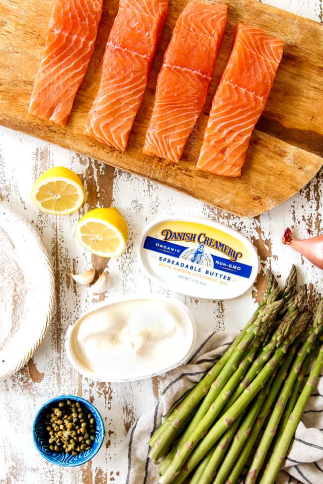 showing how to make salmon recipe by showing ingredients: salmon fillets on a cutting board, flour to dredge salmon in, butter, asparagus