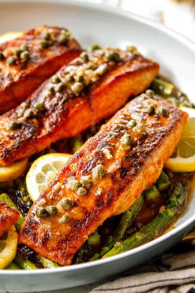 showing how to make lemon salmon and asparagus by spooning lemon butter sauce over salmon