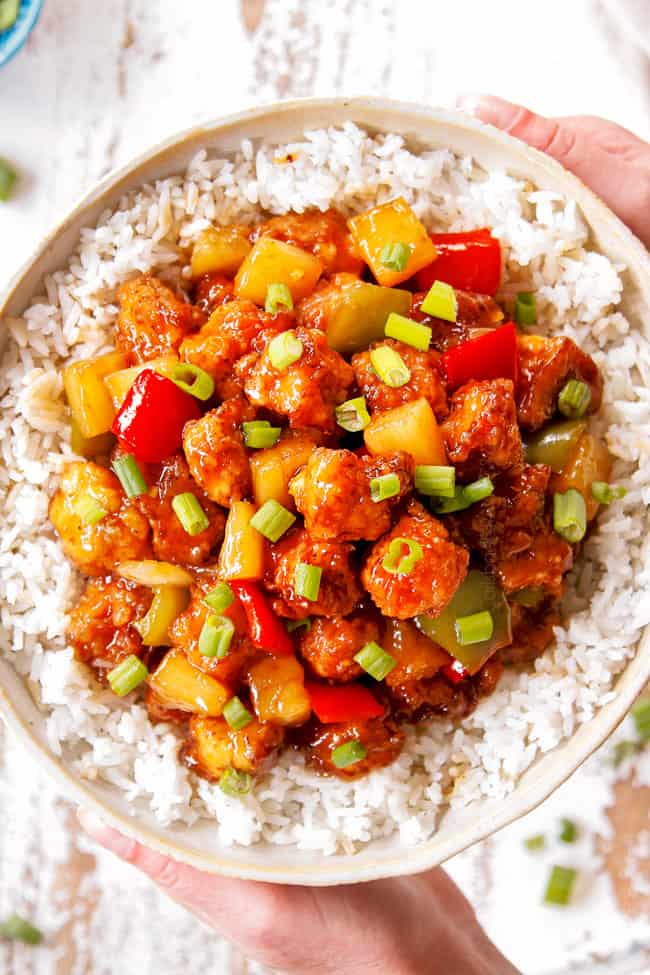 top view showing how to serve Chinese Sweet and Sour Chicken with two hands holding a bowl of chicken and rice