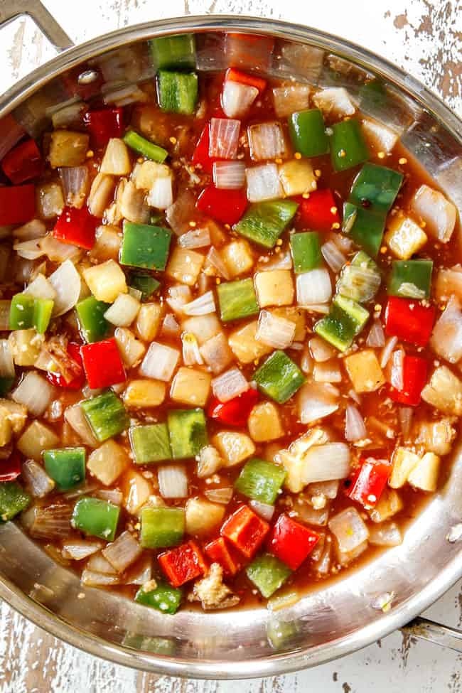 showing how to make sweet and sour chicken by adding sweet and sour sauce to vegetables and simmering until thickened