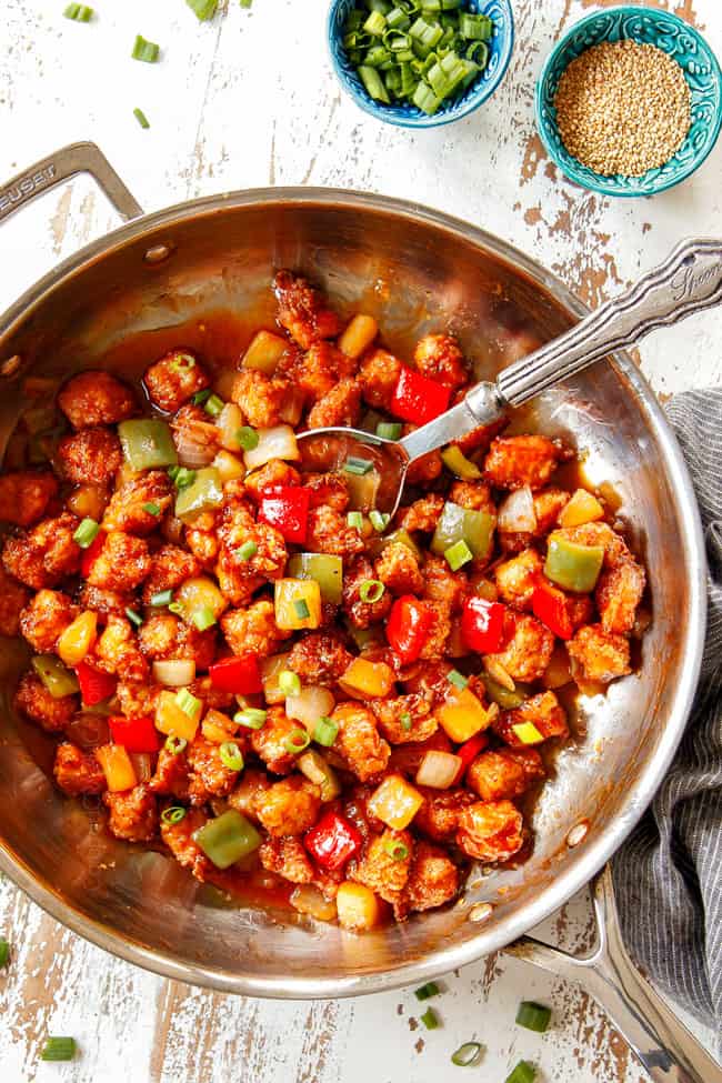 top view showing how to serve Sweet and Sour Chicken recipe by showing in a skillet with two bowls of sesame seeds and green onions