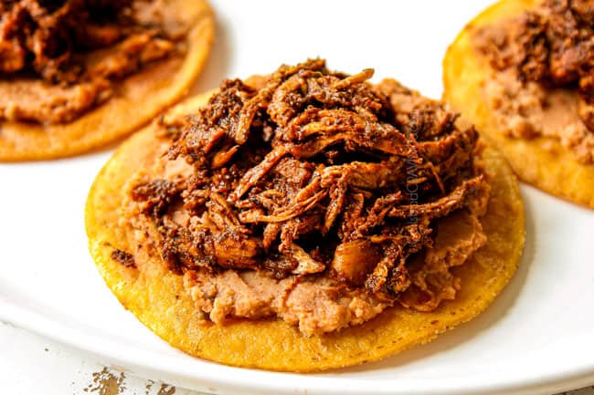 showing how to make chicken tostadas by layering tostada shells with refried beans and chicken