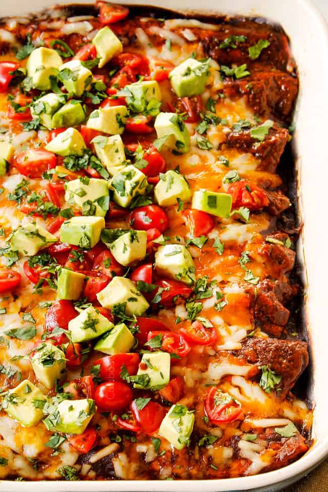showing how to top beef enchilada recipe by adding chopped tomatoes, avocado and cilantro