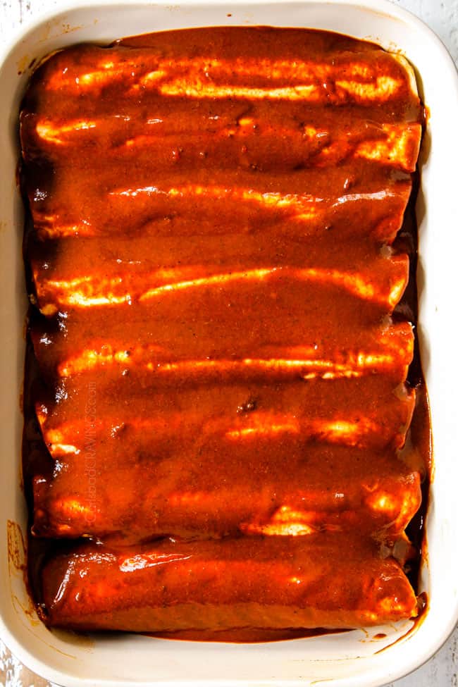 showing how to make best beef enchiladas by topping rolled tortillas in enchilada sauce