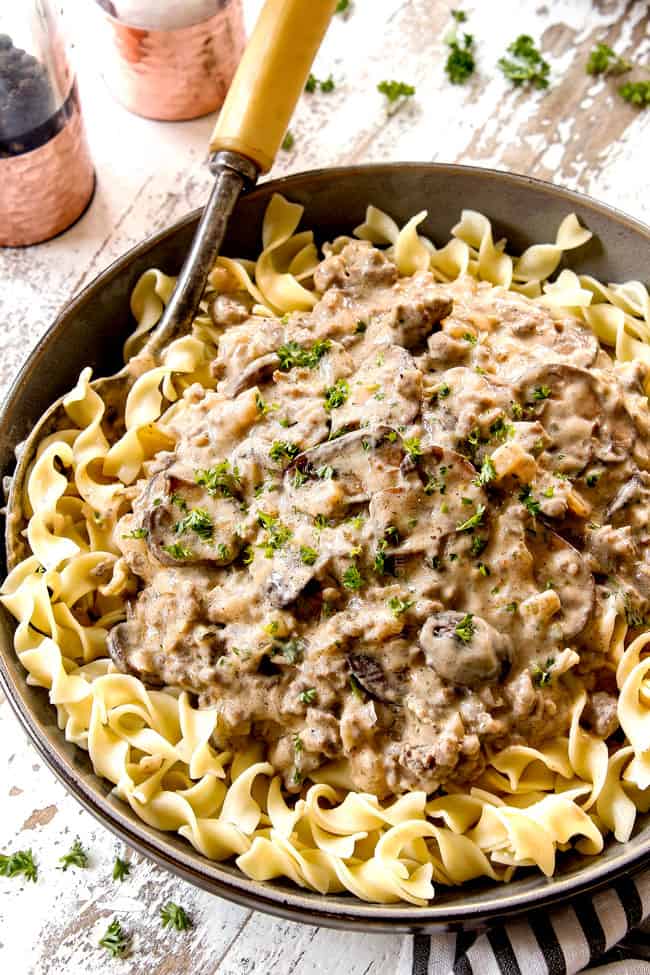 top view showing how to serve beef stroganoff with ground beef by add egg noodles to a bowl, topping with creamy mushroom gravy and garnishing with parsley