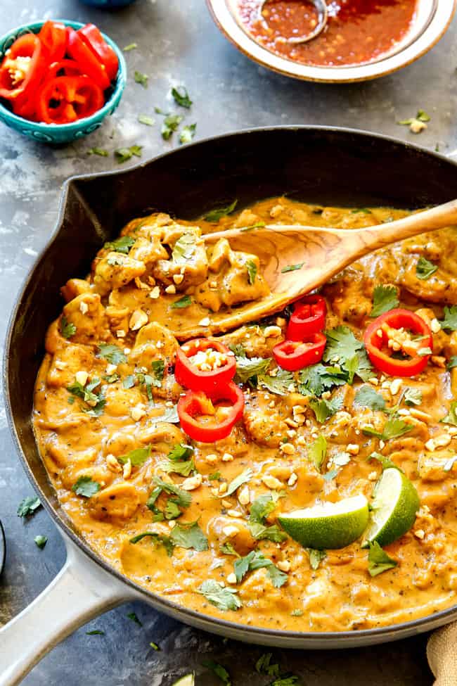 side view of peanut sauce chicken in a skillet showing how to garnish with cilantro, red chilis and lime juice