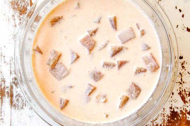 showing how make chicken nuggets recipe by marinating chicken in buttermilk in a glass bowl