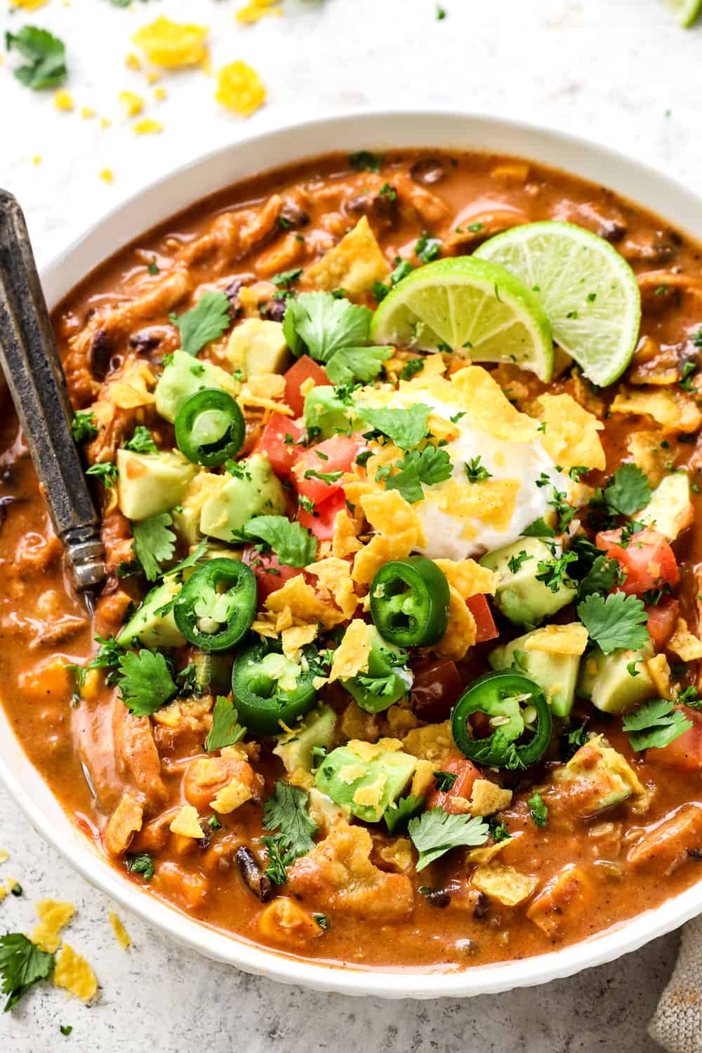 showing how to make Chicken Enchilada Soup recipe by serving with toppings: sour cream, jalapenos, cilantro, avocados, lime juice and crushed tortilla chips