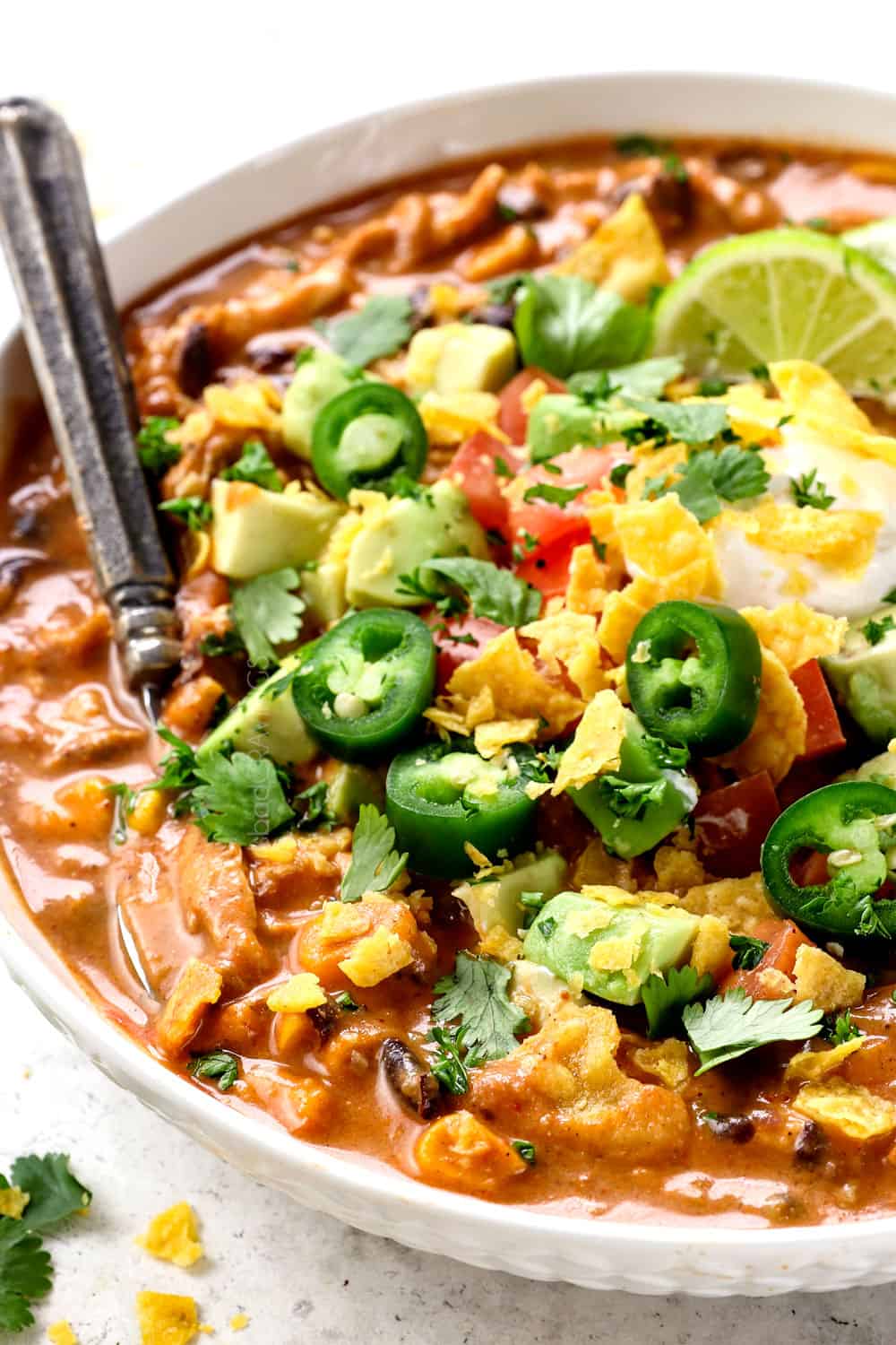 showing how to garnish Chicken Enchilada Soup recipe by topping with avocados, tomatoes, cilantro and tortilla chips