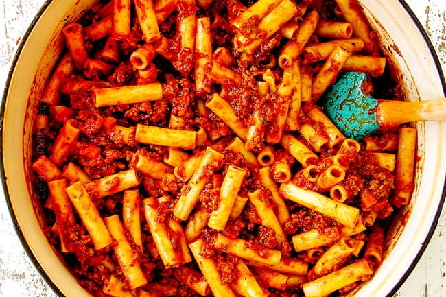 showing how to make best Baked Ziti recipe mixing the ziti pasta with the meat sauce