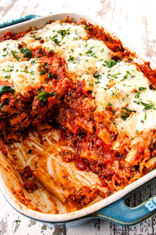 showing how saucy Baked Ziti with ricotta, Italian sausage and meat is by scooping away half of the pasta and showing the layers of noodles and sauce