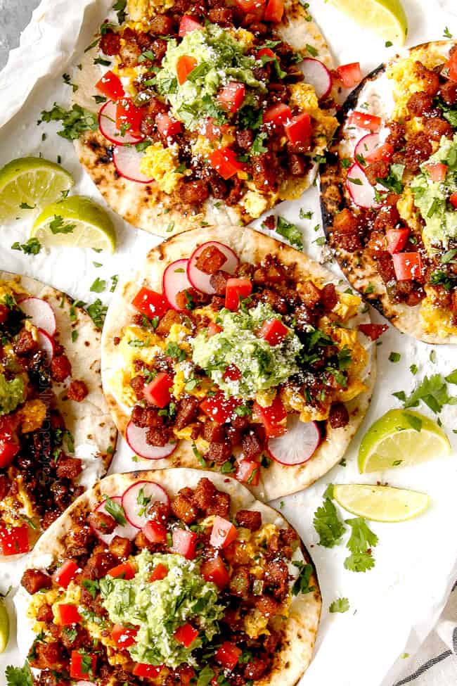 top view of breakfast taco recipe on a white tray showing what's in breakfast tacos with flat tortillas layered flat layered with chorizo,potatoes, scrambled eggs and tomatoes