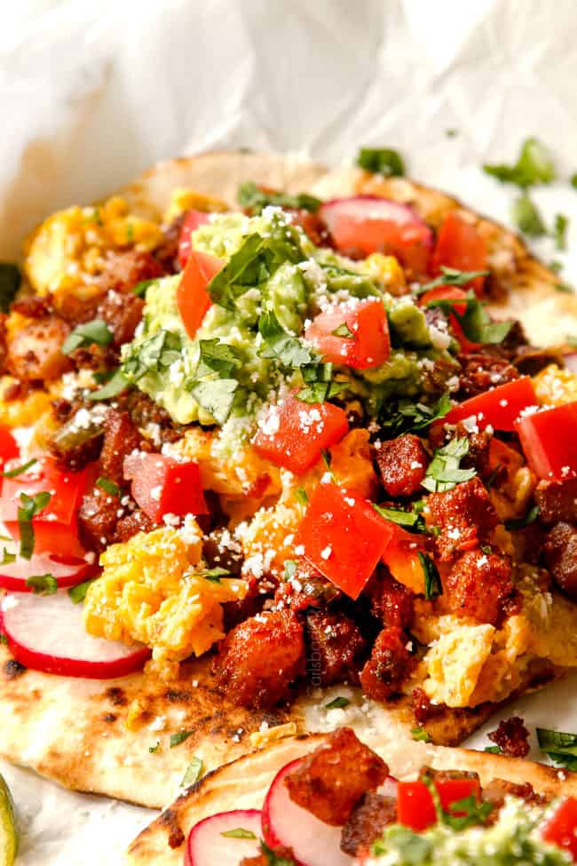 showing how to make breakfast taco recipe by spreading some sour cream or Greek yogurt down the center of the tortillas then topping with eggs, salsa, guacamole, radishes, cilantro, hot sauce.