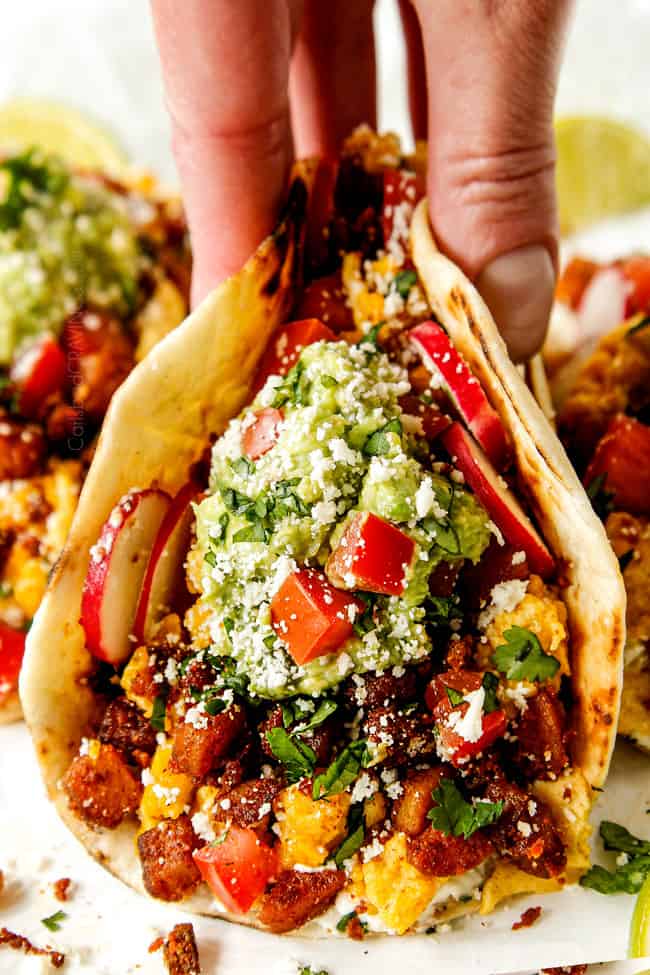 up close showing how to serve breakfast tacos by topping with guacamole and tomatoes