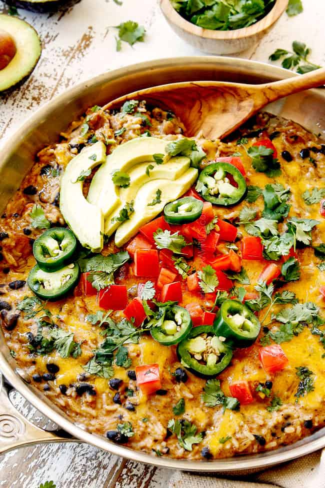 showing how to serve Green Chili Chicken and rice by topping with cilantro, jalapenos and avocados and scooping with a wood spoon