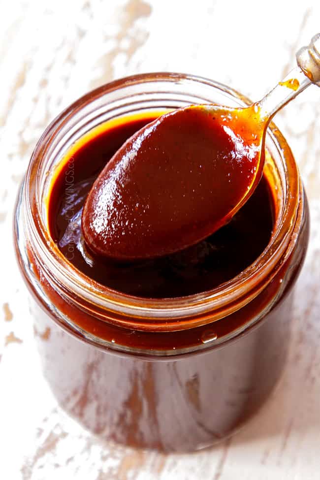 BBQ Sauce recipe is in a glass mason jar with a spoon dipping into the sauce to show rich and thick it is