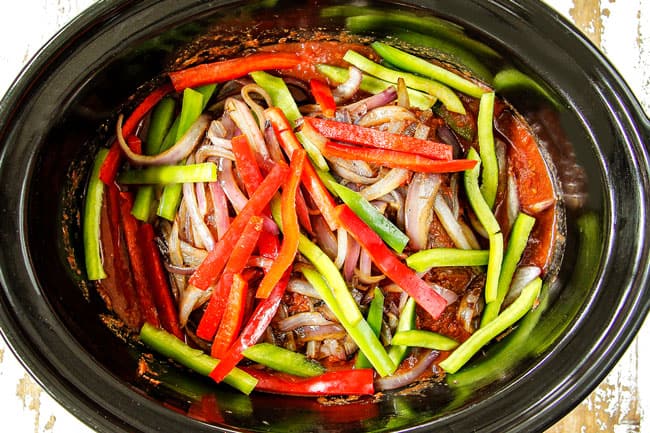 showing how to make Slow Cooker Ropa Vieja by adding beef, tomatoes, beef broth, oregano, cumin, onions and bell peppers to crockpot
