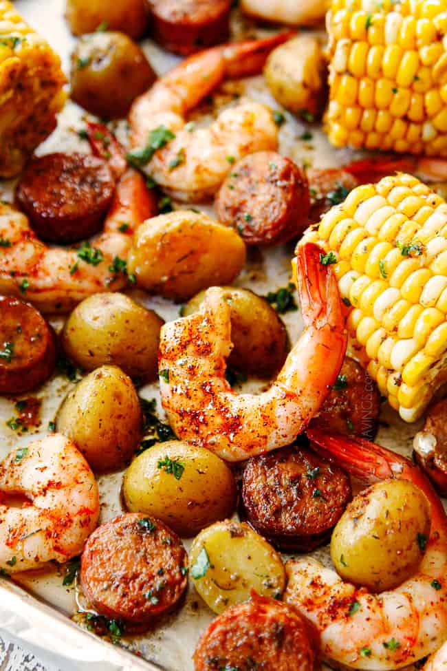 showing how to season shrimp boil recipe by adding sprinkling Old Bay seasoning over the sheet pan