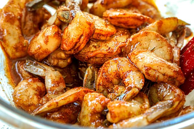 showing how to make jerk shrimp by tossing shrimp with jerk seasonings in a glass bowl