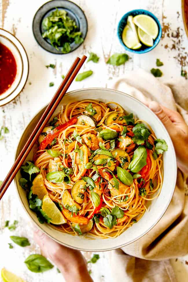 showing how to serve rice noodles recipe with a top view of two hands holding a white bowl of rice noodles and chopsticks.