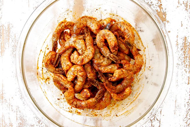 showing how to make grilled shrimp recipe by adding shrimp to a glass bowl and stirring to combine with marinade