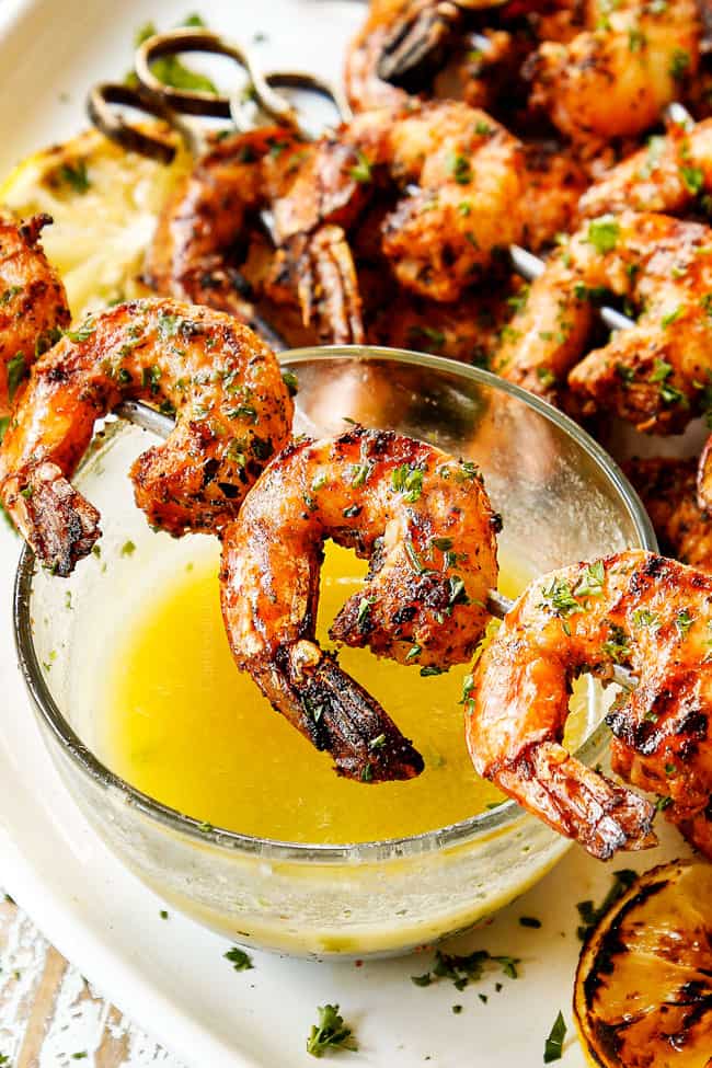showing how to serve grilled shrimp skewers by placing skewer on a bowl of melted butter to dip in