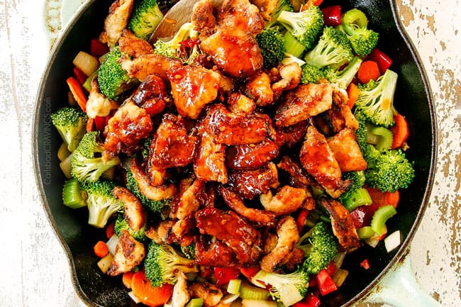 showing how to make Hunan chicken by adding Hunan sauce to skillet with stir fried veggies