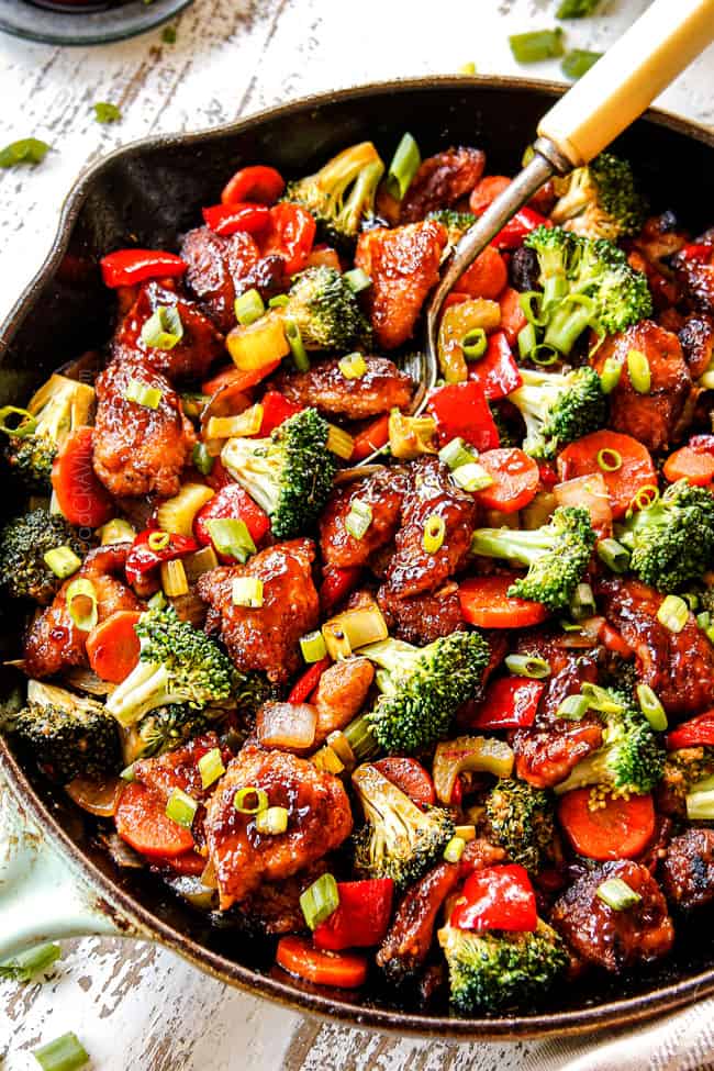 showing how to serve Hunan Chicken by scooping up with a metal spoon from a cast iron skillet