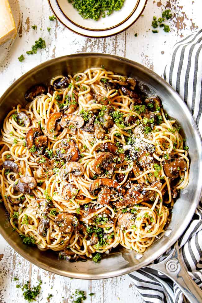 showing how to garnish creamy Mushroom Pasta in a stainless steel skillet by topping with parley and Parmesan