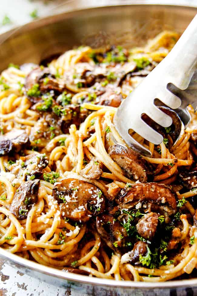 showing how to serve Mushroom Pasta recipe in a stainless steel skillet by twirling with tongs