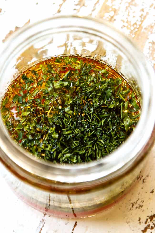 showing how to make reek orzo pasta by adding olive oil, lemon juice, red wine vinegar and dill o a glass jar and shaking