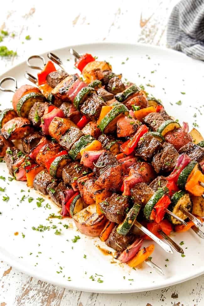 showing how to garnish steak kabobs with bell peppers, onions and zucchini by sprinkling skewers with parsley