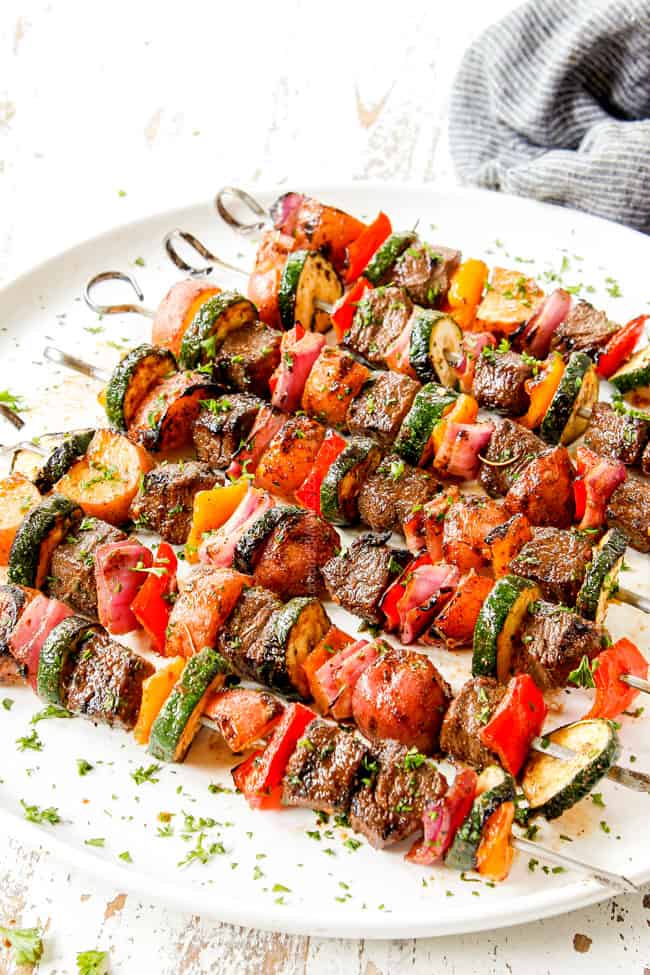 showing how to serve beef kabobs by lining on a plate and garnishing with parsley
