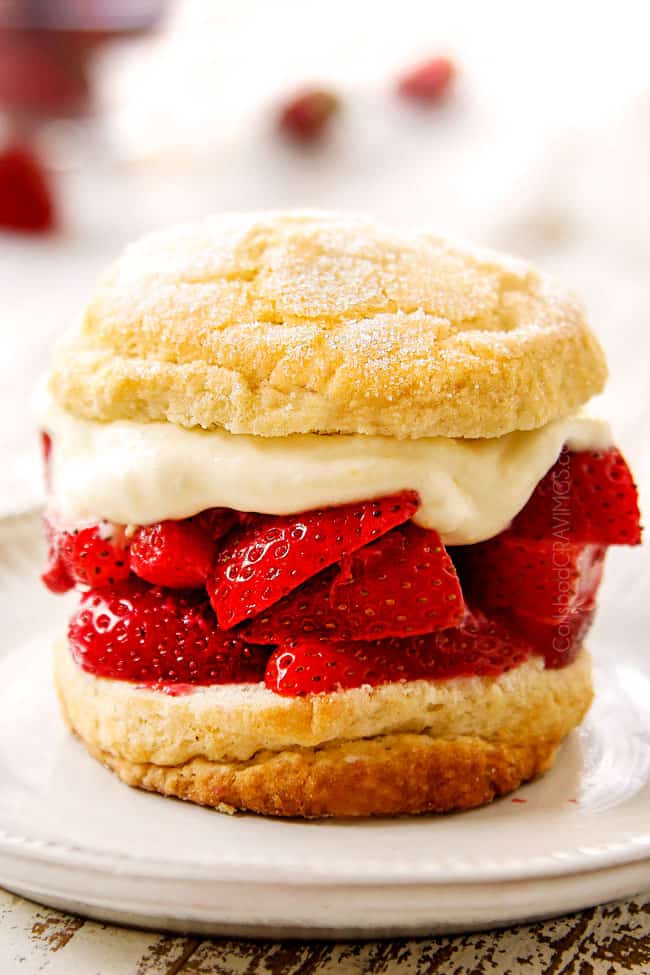 showing how to make strawberry shortcake by adding whipped cream on top of strawberries and topping with a biscuit