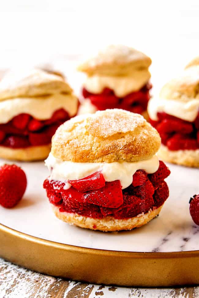 showing how to serve strawberry shortcake by layering biscuits with strawberries, whipped cream and topping with half a biscuit