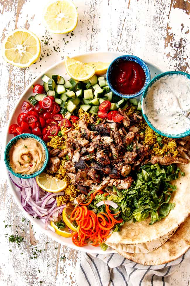 top view of doner kebab plate with thinly sliced meat, thinly sliced lettuce, thinly sliced red onions, chopped tomatoes, chopped cucumber, Lebanese flatbread and garlic yogurt sauce