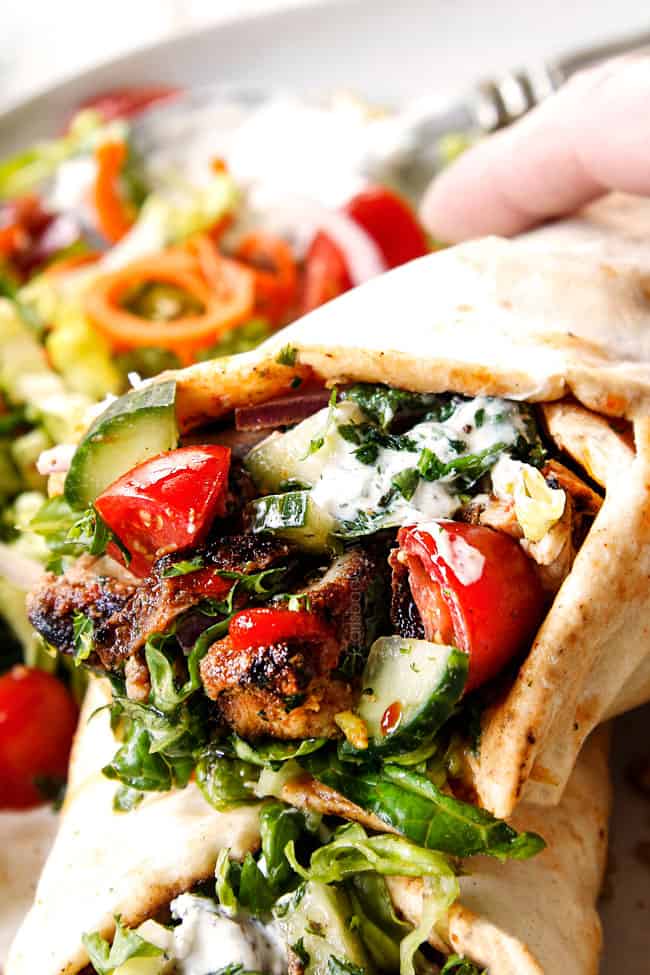 up close of doner kebab wraps with thinly sliced meat to Lebanese flatbread with hummus, thinly sliced lettuce, thinly sliced red onions, chopped tomatoes, chopped cucumber, chili sauce and garlic yogurt sauce
